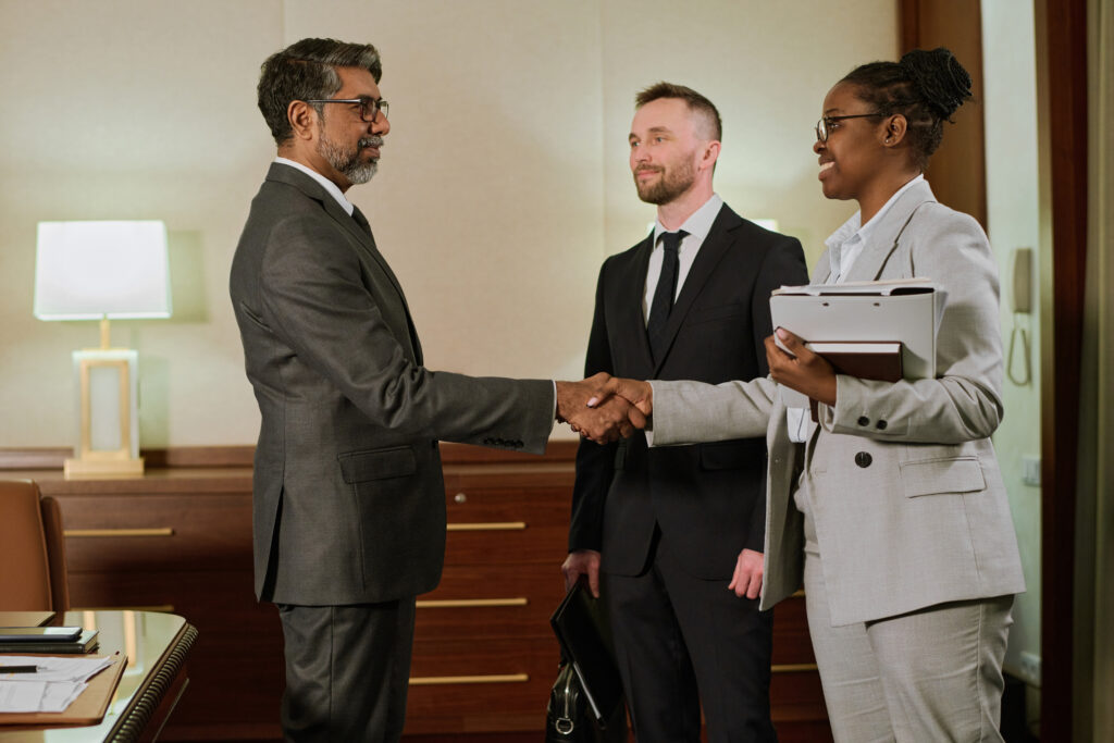 Happy young African American businesswoman with folder and notebook shaking hand of confident mature male director of company